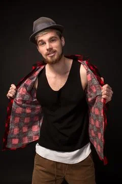 Handsome trendy young guy at the studio on black background. He wears beard and Stock Photos