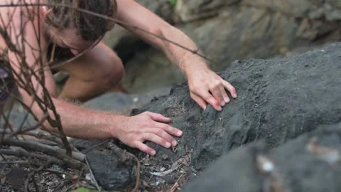 A handsome white-skinned man with bare breasts climbs a rock with tension. Video stock 234021663