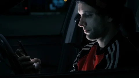 Handsome white young man uses a phone while sitting in a car in the evening. Stock Footage 117263248