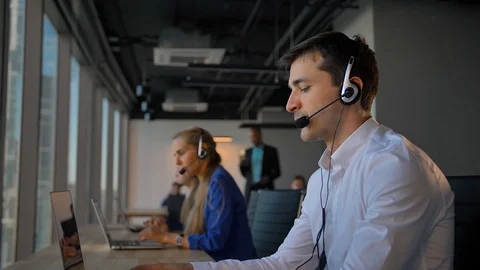 Handsome worker in headset calling to cuctomers in business office call center Stock Footage 96989081