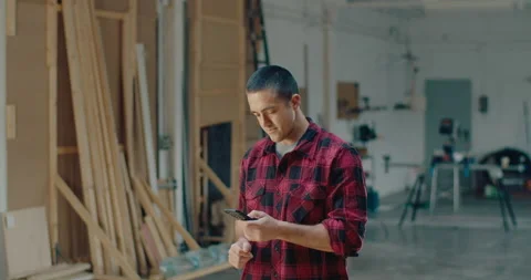 Handsome worker using a smartphone while smiling and standing in the workshop Stock-Footage 199620217