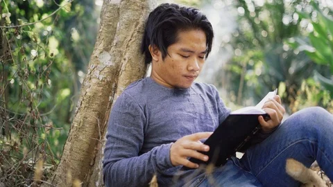 Handsome young Asian man reading a book at park with fresh nature background. Stock Footage 93493702