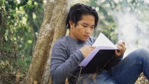 Handsome young Asian man reading a book at park with fresh nature background. Stock Footage 93497445