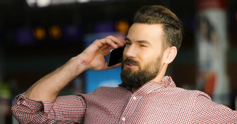 Handsome young attractive man sitting and talking on the phone at the airport of Stock Footage 77523785