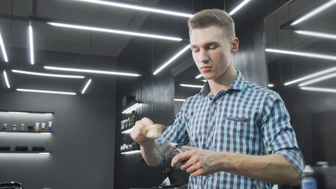 Handsome young barber smiling to the camera while cleaning his clipper Video stock 116970938