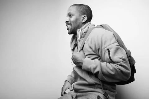 Handsome young black man with backpack posing over white wall. Black and white. Fotos de archivo
