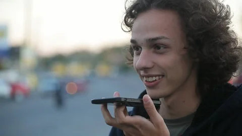 Handsome young boy talking in voice chat on the phone on the street Vidéo 97409385