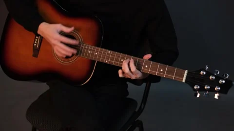 A handsome young brunet man playing guitar while sitting on a chair in a dark st Stock Footage 320356089