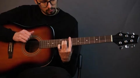 A handsome young brunet man playing guitar while sitting on a chair in a dark st Stock Footage 320356104