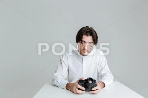 Handsome young brunette man sitting at the table holding camera Stock Photos