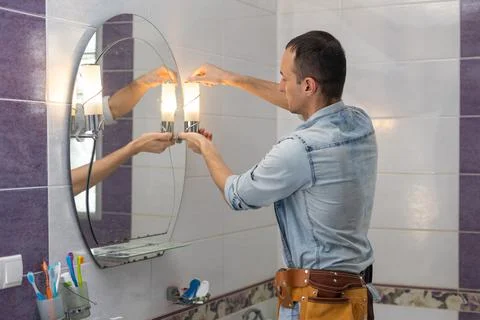 Handsome young builder is twisting the light bulb in. The man is looking up. Stock Photos
