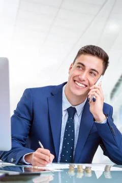Handsome young  businessman talking on smart phone in office. Stock Photos