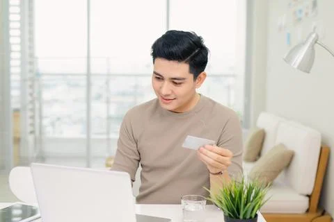 Handsome young businessman using a computer while holding a credit card in an Stock Photos