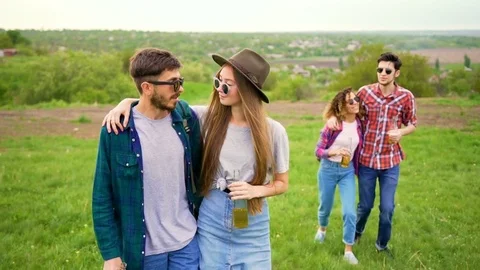 Handsome young couples walks in the park, holding bottles with drinks  Stock Footage 75694752
