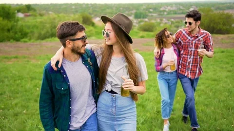 Handsome young couples walks in the park, holding bottles with drinks  Stock Footage 75694756