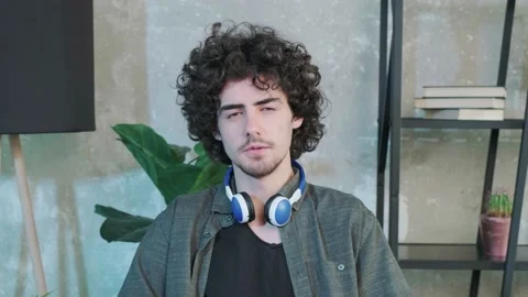 Handsome young curly haired guy looking at the camera and trying to explain Stock Footage 155640463