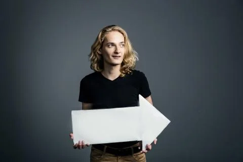 A handsome young guy with long blonde hair and a smile face holds a white arr Stock Photos
