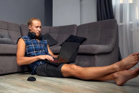 Handsome young guy working with a computer remotely sitting on the floor next to Stock Photos