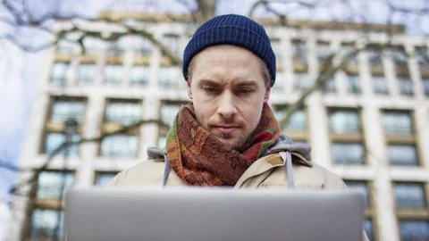 Handsome young hipster male using his laptop outdoors in the city Stock Photos