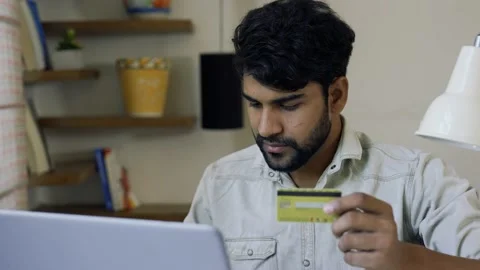 Handsome young Indian man using laptop at home and holding credit card. 스톡 동영상 155576934