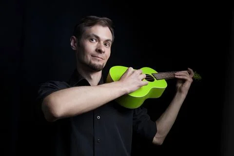 Handsome young low key man portrait with fun green ukulele guitar over black Stock Photos