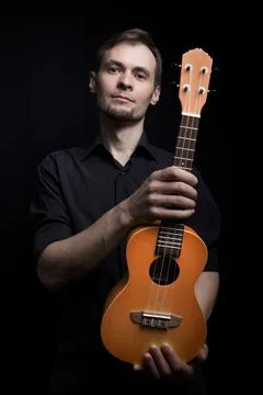 Handsome young low key man portrait with ukulele guitar over black background Stock Photos