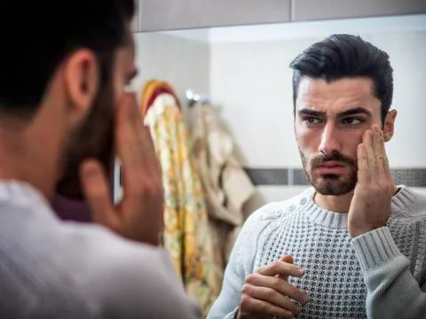 Handsome young man applying moisturizing cream on face Stock Photos