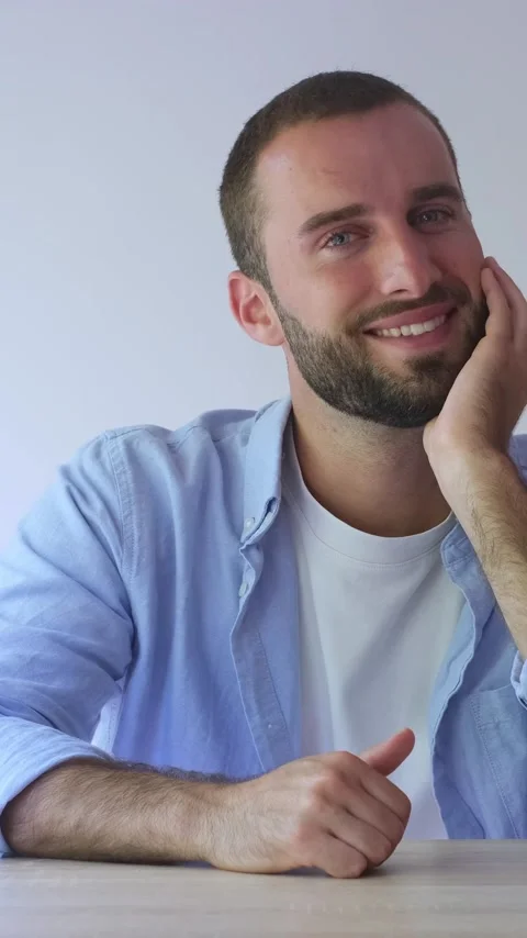 Handsome young man with a beard and blue eyes sitting at a wooden table on a Vídeos de archivo 344757183