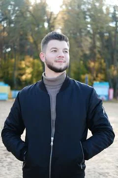 Handsome young man with a beard and in a black jacket posing on the beach. Sl Stock Photos