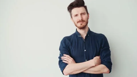Handsome young man with a beard in a blue shirt folded his arms on his chest and Stock Footage 197182400