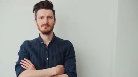 Handsome young man with a beard in a blue shirt folded his arms on his chest and Stock-Footage 197182438