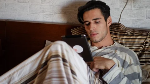 Handsome young man in bed typing on tablet PC Stock Footage 87678099