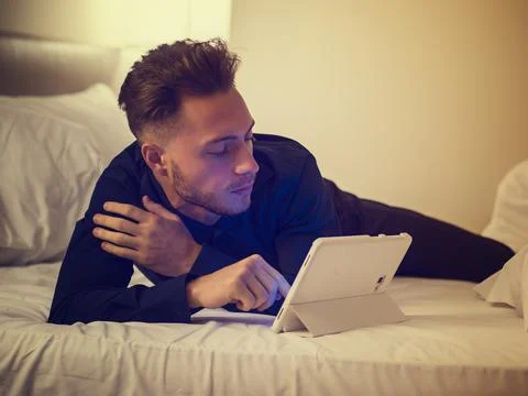 Handsome young man in bed typing on tablet PC Stock Photos