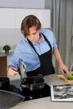 Handsome young man checking a pot at a kitchen Stock Photos