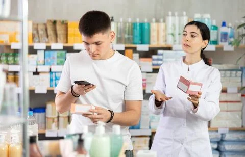 Handsome young man choosing box with pills in pharmacy, scan QR code on label Fotos de archivo