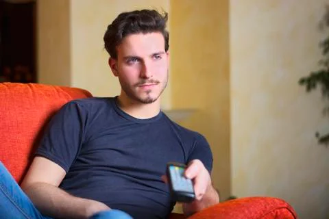 Handsome young man on counch, using tv remote control Stock Photos