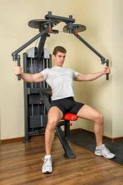 Handsome young man does workout at chest fly machine in gym Stock Photos