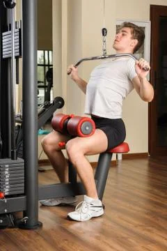 Handsome young man doing b lats pull-down workout in gym Stock Photos