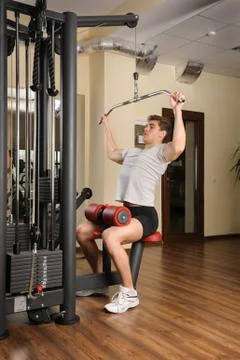 Handsome young man doing b lats pull-down workout in gym Stock Photos