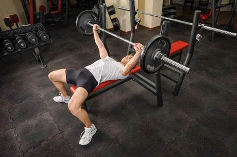 Handsome young man doing bench press workout in gym Stock Photos