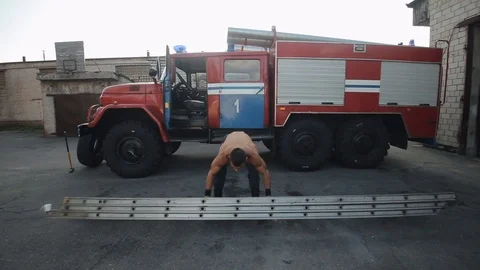 Handsome young man doing exercises with a metal ladder in front of a fire engine Video stock 120507329