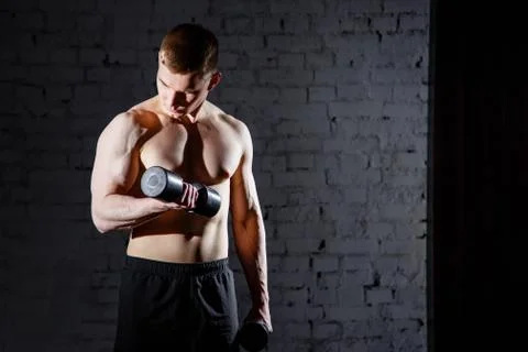 Handsome young man doing exercises for the biceps against a brick wall. Stock Photos