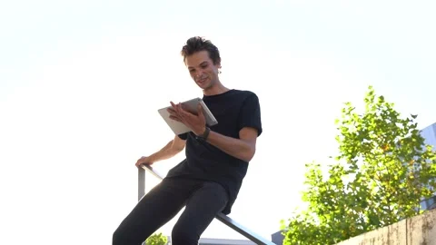 Handsome young man doing video call on digital tablet while sliding down railing Stock Footage 136981744