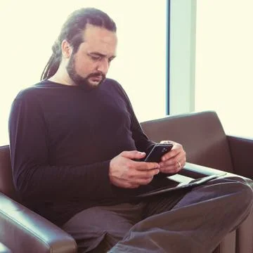 Handsome young man with dreadlocks using his phone at an airport lounge Stock Photos