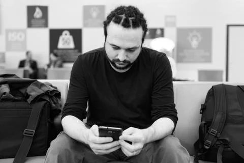 Handsome young man with dreadlocks using his phone at an airport lounge. Stock Photos