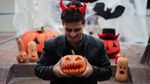 Handsome Young man dressed as a vampire devil with makeup holds a pumpkin Jack O Stock Footage 219814153