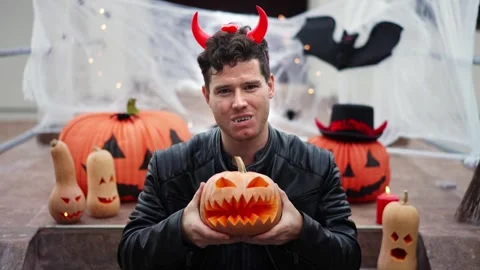 Handsome Young man dressed as a vampire devil with makeup holds a pumpkin Jack O Stock Footage 250410261