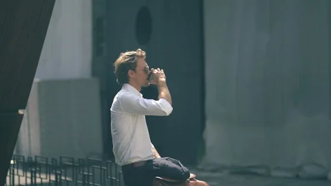 Handsome Young Man Drinking Coffee Sitting On The Metal Railing Stock Footage 126127923