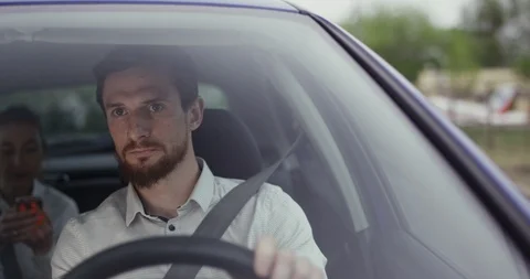 Handsome young man driving a car with passanger on back seat Stock Footage 107547577