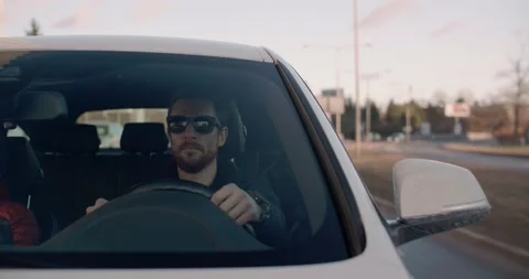 Handsome young man driving a car with passanger on back seat Stock Footage 229695589